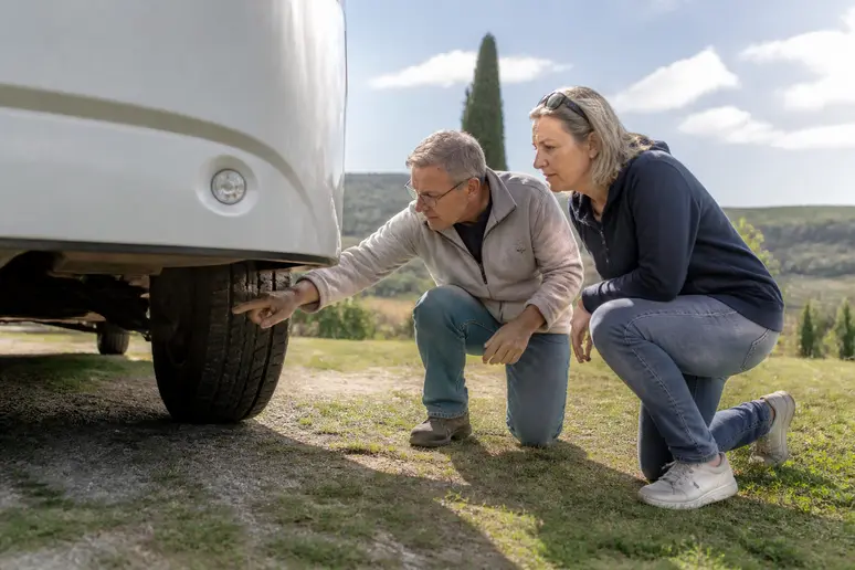 Un couple français examine attentivement le châssis d'un camping-car Benimar d'occasion dans un paysage rural ensoleillé.