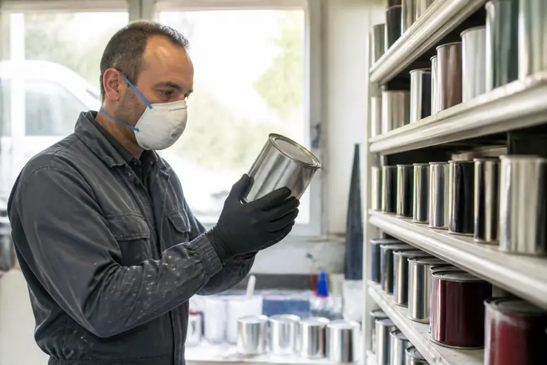 Un homme en atelier mécanique choisit une peinture pour voiture, évaluant les différentes options disponibles pour sa carrosserie.