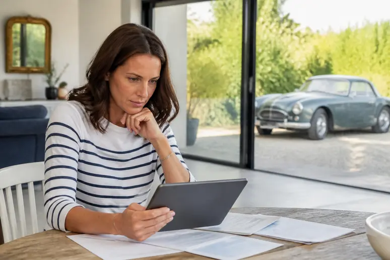 Femme comparant des contrats d'assurance voiture ancienne sur sa tablette, dans un salon lumineux.