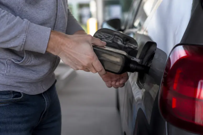 Une personne verse un additif diesel dans le réservoir d'une voiture dans une station-service française en plein jour.