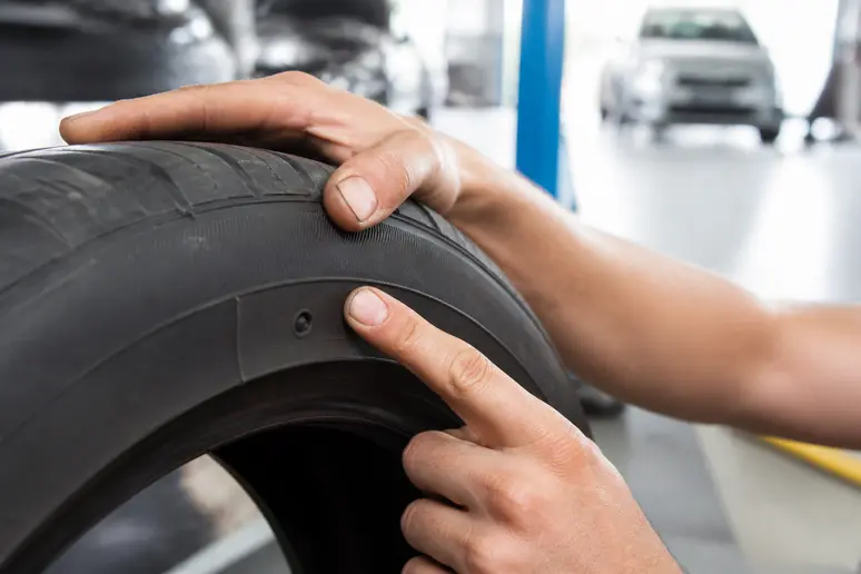 Mains lisant les dimensions et les inscriptions techniques sur le flanc d'un pneu de voiture
