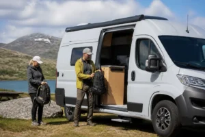 Un camping-car compact stationné dans un cadre naturel avec un couple préparant le matériel, illustrant le Dacia Sandman prix.