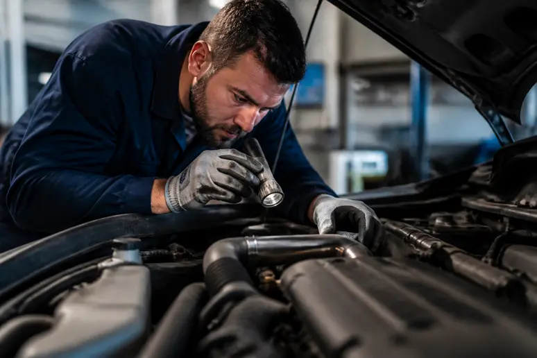 Mécanicien inspectant le compartiment moteur d'un véhicule d'occasion pour vérifier l'état des pièces.