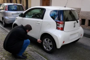 Un automobiliste inspecte une Toyota iQ avis d'occasion stationnée dans une rue urbaine