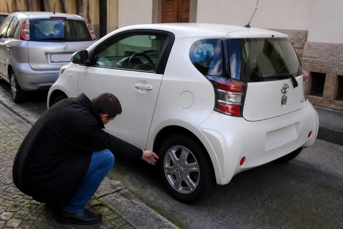 Un automobiliste inspecte une Toyota iQ avis d'occasion stationnée dans une rue urbaine
