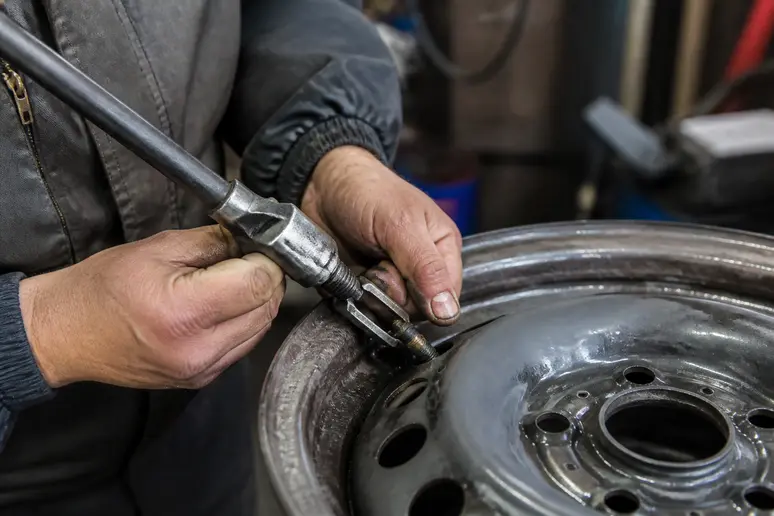 Un mécanicien installe une nouvelle valve de pneu en caoutchouc sur une jante en atelier.