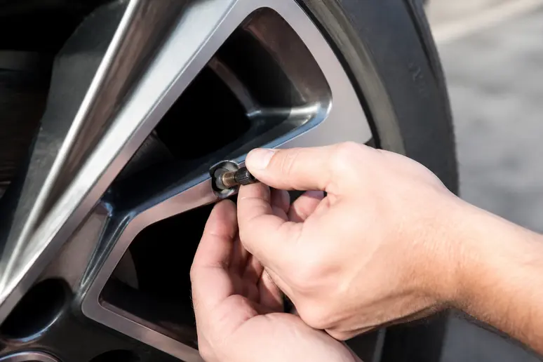 Un automobiliste revisse un bouchon de protection sur la valve de pneu d'une voiture.