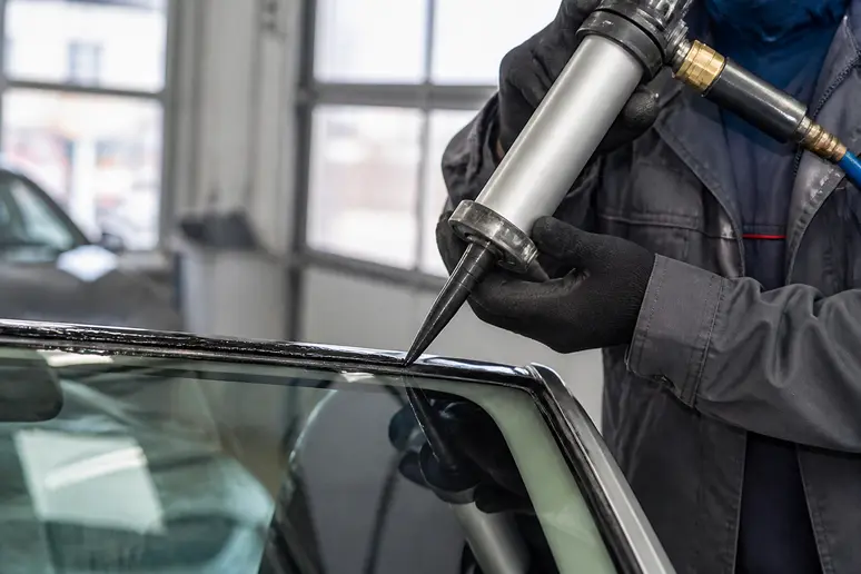 Technicien appliquant un joint de colle polyuréthane pour la pose du pare-brise