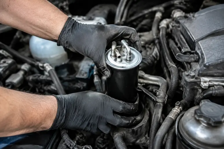 Mains d'un mécanicien installant un nouveau filtre à gasoil dans le compartiment moteur d'une voiture.