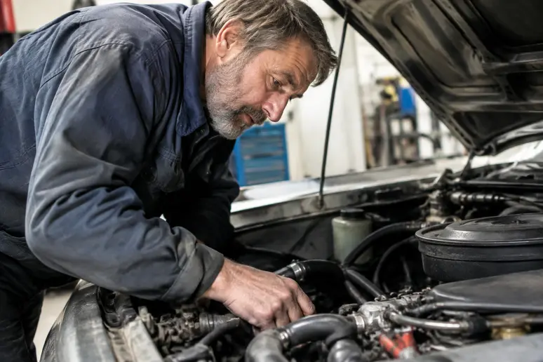 Mécanicien inspectant le compartiment moteur d'un véhicule ancien dans un atelier