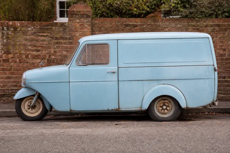 Petite camionnette bleue à trois roues garée le long d'un mur en briques rouges